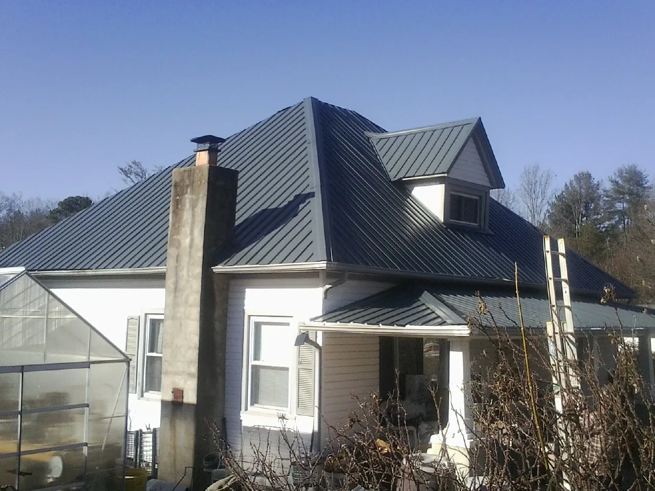 Dark blue standing seam metal roof on a white farmhouse with dormer — Slate & Tile Roof Repair by Roofing Brothers in Ellinger