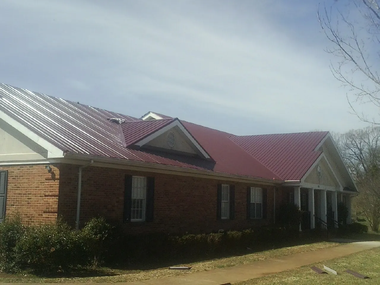 Red metal roof with gabled entries on a long brick building, from a Hail Damage Roof Repair job in Ellinger
