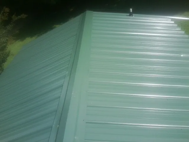 New green metal panels meeting at the ridge of a roof — Flat Roof Repair work by our crew in Ellinger