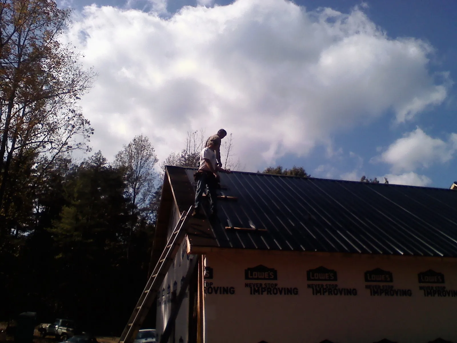 Roofer fastening dark metal panels high against a cloudy sky, from a Roof Inspection job in Ellinger